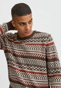 Pulover maro cu un model geometric, având dungi roșii, crem și maro închis; guler rotund și manșete cu model în vrac.