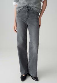 Grijze jeans met hoge taille en rechte pijpen, met subtiele vervaagde details en voorzakken. Gecombineerd met zwarte schoenen met een spitse neus.