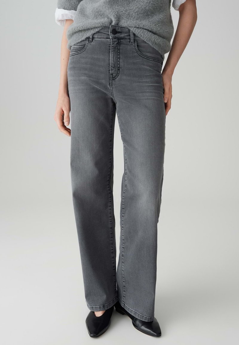 Grijze jeans met hoge taille en rechte pijpen, met subtiele vervaagde details en voorzakken. Gecombineerd met zwarte schoenen met een spitse neus.