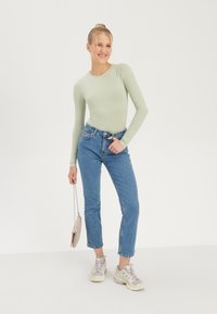 Mint green long-sleeve top paired with high-waisted blue jeans and light sneakers. Holds a small beige crossbody bag.
