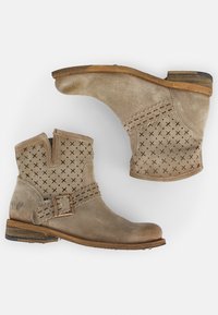 Botas de tobillo beige hechas de suave ante con detalles recortados y una correa decorativa con una hebilla de metal. Tacón bajo apilado y puntera redondeada.