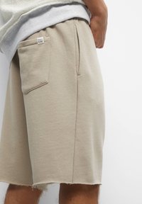 Beige cotton shorts with a casual design, featuring side pockets and a slightly frayed hem for a relaxed look.