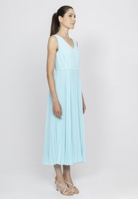 Jasnoniebieska midi sukienka w plisach z dekoltem w kształcie litery V, bez rękawów, o zwiewnej fakturze tkaniny, podkreślona beżowymi sandałkami na paski.