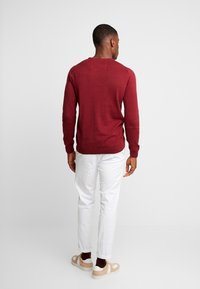 Maronfarvet sweater med rund hals og lange ærmer, parret med hvide bukser og beige sneakers. Glat tekstur, minimalistisk design.