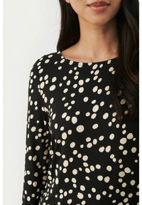 Black long-sleeve top featuring a dotted pattern in cream. The fabric appears smooth with a round neckline and a relaxed fit.