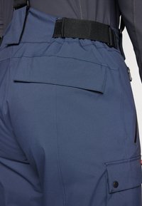 Navy cargo pants featuring a high waistband, elastic belt, and multiple pockets with flap and snap closures. Smooth texture, lightweight material.