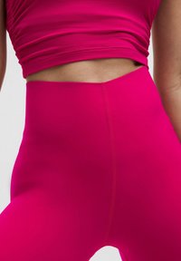 Korkeavyötäröiset legginsit kirkkaan vaaleanpunaisesta kankaasta. Suunnattoman sileä rakenne, jossa on vähän saumoja ja tiukka muotoilu.