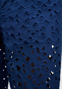 Μπλε ύφασμα με περίπλοκο μοτίβο δαντέλας λουλουδιών με κοψίματα, που δείχνει στρωματοποιημένη υφή και ανοιχτούς χώρους μέσα στο σχέδιο.