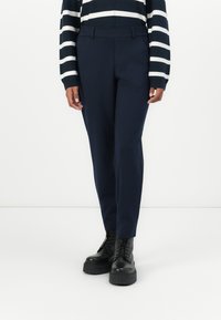 Marine skreddersydde bukser med en jevn tekstur, slim fit og beltehemper, sammen med svarte snøremotorsykkelsko. Stripete genser synlig på overkroppen.