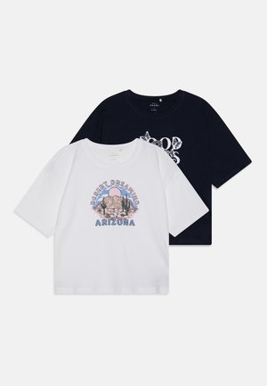Duas t-shirts de algodão: uma branca com um gráfico "Desert Dreaming Arizona", a outra azul-marinho com um design floral branco. Ambas possuem mangas curtas.