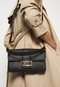 Musta teksturoitu nahkabagi kultaisella kiinnityksellä, jossa on jämäkkä muotoilu ja ohut olkahihna.