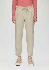Beige joggingbroek met een trekkoord in de taille, voorzien van twee voorzakken en een zijzak. Soepele textuur, taps toelopend ontwerp.