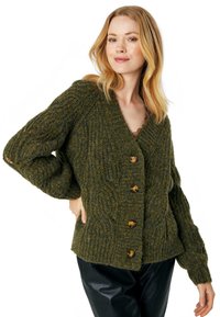 Olīvu zaļa adīta kardigāna ar teksturētu virvju rakstu, V-veida kakla izgriezumu un pieciem lieliem zelta pogām. Garas, apjomīgas piedurknes un ribota apakšmala.