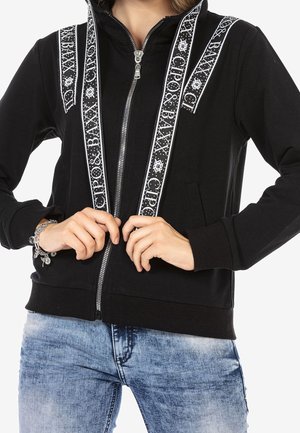 Black zip-up hoodie with white patterned trim along the shoulders and sides. Features a front zipper and two side pockets.