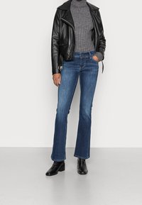 Svart läderjacka i cropped stil över en grå ribbad turtleneck, tillsammans med utsvängda mörkblå jeans och svarta klackade boots.