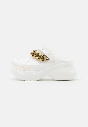 Sabot blanc avec une semelle à plateforme, comportant des trous de ventilation, un talon surélevé et un accent en chaîne dorée sur la lanière avant.