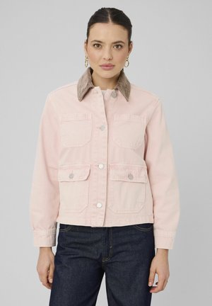 Femme aux cheveux foncés portant une veste rose clair boutonnée avec quatre poches frontales et un col en velours côtelé beige, associée à un jean bleu foncé.