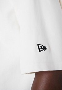 T-shirt blanc à manches courtes avec un logo noir brodé sur le poignet. Tissu en coton lisse avec une coupe classique.