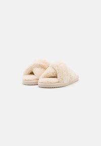 Cream-colored slippers with a plush, fur-like upper, open-toe design, and a textured sole for grip. Soft, fluffy material for comfort.