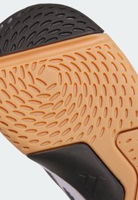 Semelle de chaussure avec une base en caoutchouc orange présentant des rainures et motifs texturés, un accent de talon noir et un bord lisse tout autour.