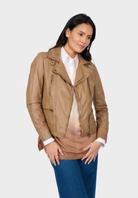 Braune Leder-Motorradjacke mit Reißverschlusstaschen, asymmetrischem Frontreißverschluss und ausgeprägtem Kragen. Der Modell trägt darunter ein weißes Hemd.