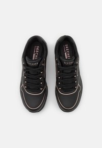 Black sneakers with perforated design, pink metallic accents, and lace-up closure. Features a cushioned insole with Skechers branding.