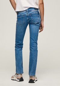 Blå denimjeans med en figursydd passform, fem fickor och lätt blekning, kombinerade med beige och grå sneakers.
