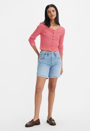 Haut à rayures rouges et blanches à manches longues avec des boutons, associé à un short en denim bleu clair. Des mocassins marron complètent l'ensemble. Look simple et décontracté.