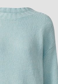 Zbliżenie na jasnoniebieski sweter dziany, ukazujące prążkowany kołnierz oraz teksturowany wzór dzianiny na ramieniu i górnej części pleców.