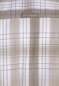 Camicia a quadri in bianco e sfumature di beige, con etichetta Columbia. Il motivo è composto da linee e quadrati alternati di diverse larghezze.