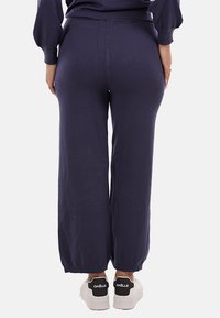 Pantaloni della tuta a gamba larga di colore blu navy, con una texture liscia. Vita elasticizzata e caviglie a costine. Abbinati a sneaker bianche con dettagli neri.