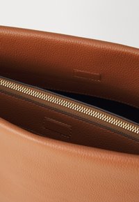 Tan leather bag interior with a gold zipper detailing. Features a smooth texture and minimalistic design. Flap closure with an inner label.