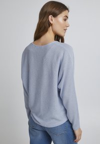 Pulover lejer, de culoare albastru deschis, cu guler rotund și umeri lăsați. Textură moale și croială relaxată, asortat cu blugi bleumarin.