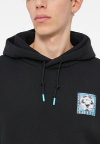 Moleton preto com cordão, apresentando extremidades azul claro. Possui um colorido patch bordado em forma de quadrado com um design de futebol no peito.