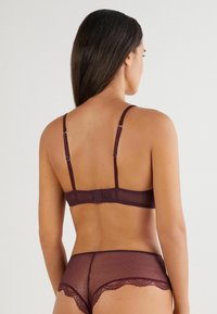 Ensemble de lingerie mauve composé d'un soutien-gorge transparent et texturé avec des bretelles réglables et d'une culotte haute transparente assortie avec des accents en dentelle.