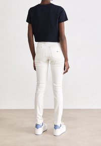 Klippt svart t-shirt, vita slim-fit jeans och vita sneakers med blå detaljer. Enkelt design, mjuk textur och standard passform.