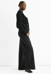 Black knit sweater with textured pattern and white studs, paired with wide-leg black denim jeans and black shoes with a strap detail.