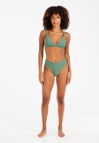 Žalias juostelėmis bikini komplektas, turintis trikampį viršų su plačiomis petnešėlėmis ir aukštu liemeniu. Medžiaga turi subtilų raštą ir tekstūrą.
