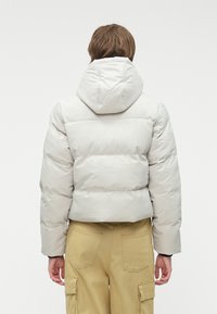 Kurtka ocieplana w jasnoszarym kolorze z kapturem. Charakteryzuje się skróconą sylwetką, pikowanymi sekcjami oraz gładką, błyszczącą teksturą.