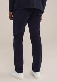 Mörkblå kordflodbyxor med rak bendesign, som har en mjuk textur och elastisk midja. Matchas med vita sneakers.