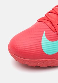 Red athletic shoe with textured upper, featuring a mint green Nike swoosh logo and rubber sole with a patterned grip design.