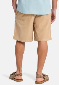 Χακί βερμούδα από κορντόρι με δύο πίσω τσέπες, ευθεία κοπή και διακριτική ραβδωτή υφή. Συνδυασμένο με καφέ ρυθμιζόμενα σανδάλια.