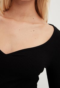 Schwarzes geripptes Oberteil mit weit ausgeschnittenem V-Ausschnitt und langen Ärmeln, aus einem strukturierten Stoff und mit taillierter Passform. Glatte Oberfläche, minimales Design.