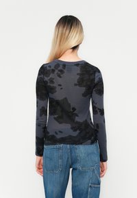 Camisa de manga larga en gris oscuro con un patrón abstracto negro. Fabricada en material suave, cuenta con un cuello redondo y un corte entallado.