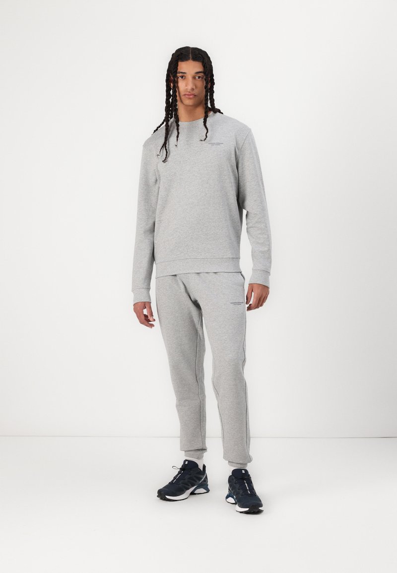 Grey sweatshirt and sweatpants set, made from soft fabric, featuring ribbed cuffs and a simple crew neck design. Worn with black athletic shoes.