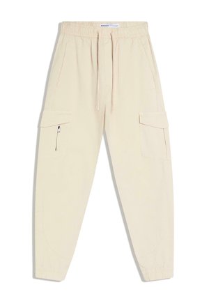 Beige Cargo-Jogginghosen mit elastischem Bund, Kordelzug, seitlichen Klappentaschen, Reißverschlusstasche am linken Bein und elastischen Fußbündchen.