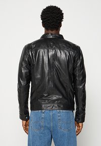 Schwarze Lederjacke mit glatter Textur, klassischem Kragen und Rückenähten. Kombiniert mit Jeans, was einen lässigen Look zeigt.