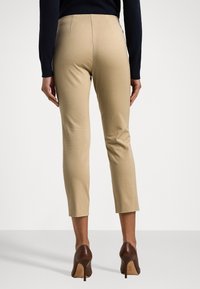 Slim-fit beige trousers with a mid-rise waist and cropped leg, made of smooth fabric. Paired with brown high-heeled shoes.