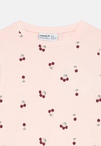 Jasnoróżowa bawełniana koszula z drobnymi, ciemnoczerwonymi nadrukami wiśni i zielonych liści. Posiada prążkowany okrągły dekolt i miękką fakturę.