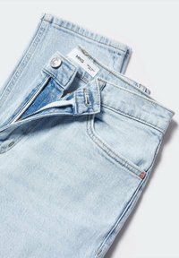 Jean en denim bleu clair avec une braguette et un bouton ouverts, montrant une étiquette blanche à l'intérieur de la ceinture.